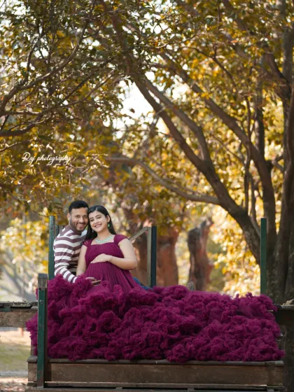 A beautiful couple's portrait in a park-like setting. The mother-to-be is wearing a wine-colored ruffled gown.