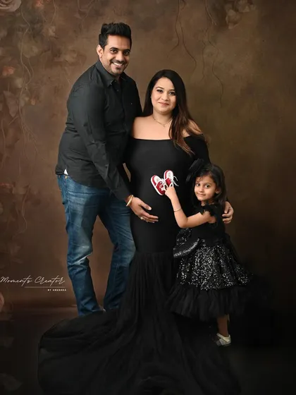 A complete family portrait in classic black. The older daughter holds tiny shoes, a sweet nod to the new baby joining their family soon.