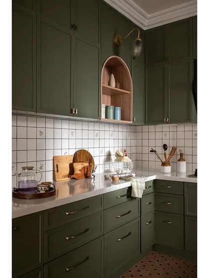 This kitchen is designed to feel both classic and soulful. I chose olive green for the cabinets, paired with brass handles and hand-painted backsplash tiles for a personal touch. An archway from the dining area frames the view, while a smaller arched niche inside provides a charming display space, connecting the rooms beautifully.