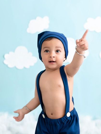 A baby boy in a blue hat points upward during his sky-themed photoshoot.