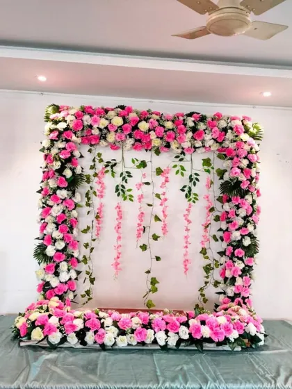 A lovely pink and white themed decoration for a home Ganpati celebration. We used hanging strings of pink flowers against a backdrop of green leaves to create a delicate and charming effect within the floral frame.