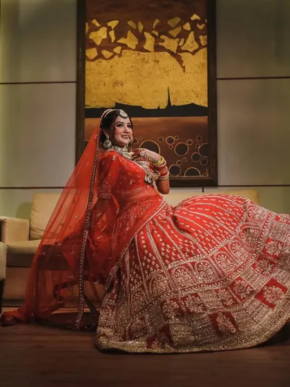A full-length portrait of the bride seated, her magnificent red lehenga spread around her. This shot emphasizes the grandeur and regality of her bridal outfit.