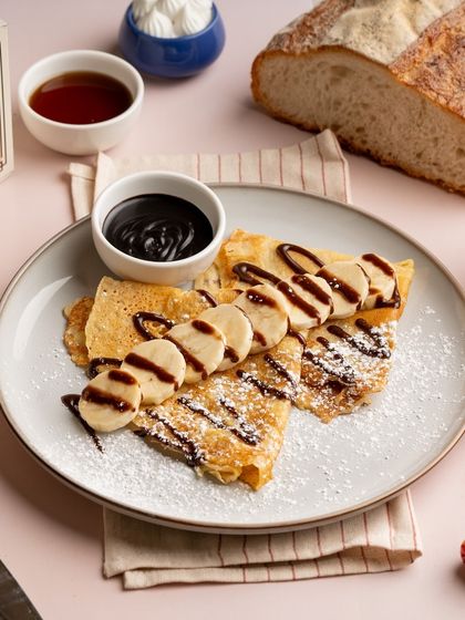 I also make classic French crepes. Here they are served simply with sliced bananas and a generous drizzle of chocolate sauce, perfect for breakfast or dessert.