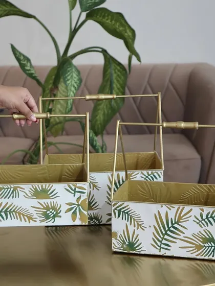 A set of three metal baskets with a white and green leaf print and elegant gold handles. These are perfect for organizing your home or as a stylish base for a gift hamper.
