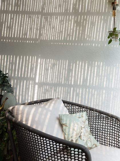 A sunny sit-out with comfortable cane furniture. The light filtering through the bamboo screen creates a beautiful, striped pattern, making this a favorite spot for morning coffee.