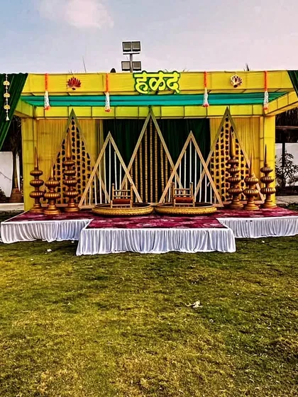 A grand outdoor Haldi stage with a green and yellow theme, featuring ornate seating and a backdrop of geometric wooden frames.