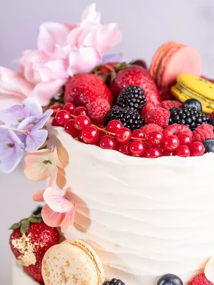 A close-up of the top tier, showing the beautiful arrangement of summer berries, macarons, and edible gold leaf.