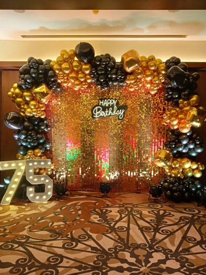 An elegant 75th birthday celebration with a gold sequin backdrop. The decor is accented with black and gold balloons and large marquee numbers, creating a luxurious feel.