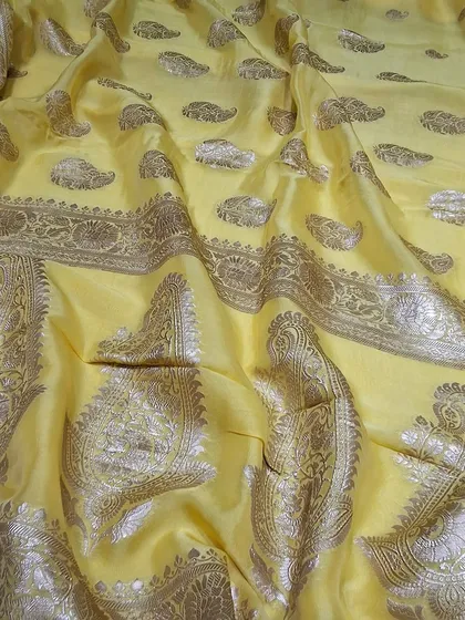 A soft yellow Banarasi saree with intricate paisley motifs. The fabric has a beautiful sheen that catches the light, making it a subtle yet stunning choice for any special occasion.