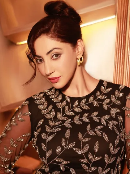 An elegant evening portrait of actress Reyhna Pandit in a sophisticated black dress with silver embroidery. The warm lighting and refined setting highlight a moment of pure glamour.