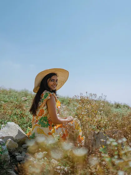A bride-to-be smiles in a sunlit field, capturing a moment of quiet happiness during her Mussoorie pre-wedding shoot.