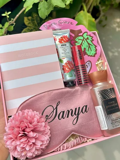 A perfectly pink and personalized hamper for a dear friend. This gift box includes a custom "Sanya" eye mask, a striped notebook, a mini shower gel, and other skincare treats.