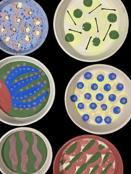 A collection of freshly painted plates, each with a different bold, graphic pattern. This is the exciting stage before glazing, where the designs are vibrant and full of promise.