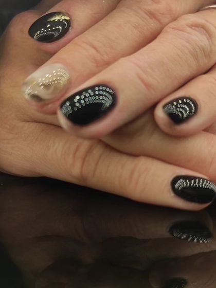 A unique black manicure with intricate, dotted silver patterns.