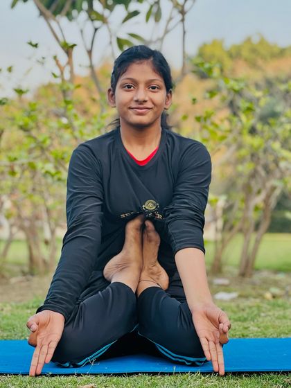 The Kandpīḍāsana, a challenging pose that requires flexibility in the hips and spine. This young yogini holds it with a calm and steady gaze.