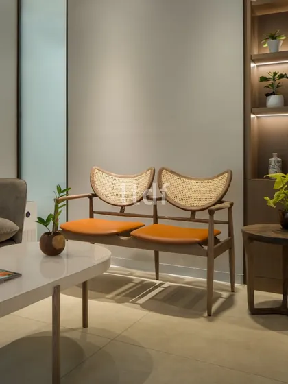 The waiting area features a mix of comfortable seating options, including a sofa and a wooden bench with cane detailing. The use of natural materials and a calm color palette creates a welcoming and relaxing atmosphere for patients.