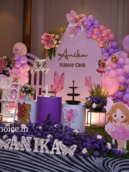 A beautiful fairy and butterfly themed setup in shades of purple and pink. This decor includes custom fairy cutouts, floral arrangements, and a cascading balloon garland for a magical first birthday.