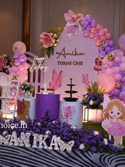A beautiful fairy and butterfly themed setup in shades of purple and pink. This decor includes custom fairy cutouts, floral arrangements, and a cascading balloon garland for a magical first birthday.