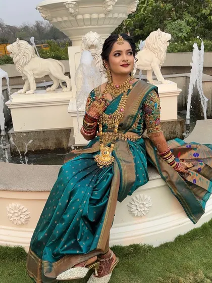 A regal portrait of the bride seated by a fountain in her teal Nauvari.