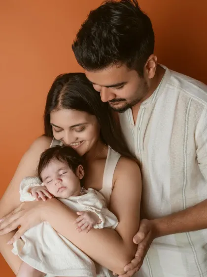 A warm and loving portrait of a new family. The earthy orange backdrop and soft white outfits create a cozy and intimate feel for their first photoshoot together.