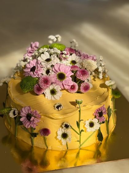A close-up of one of my favorite floral cakes. The butter-yellow frosting is the perfect canvas for an arrangement of fresh, colorful daisies and chrysanthemums, creating a vibrant, garden-inspired look.