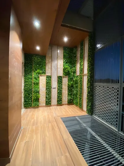 The same Faridabad balcony wall seen at night, with integrated lighting that highlights the textures of the wood, stone, and greenery.