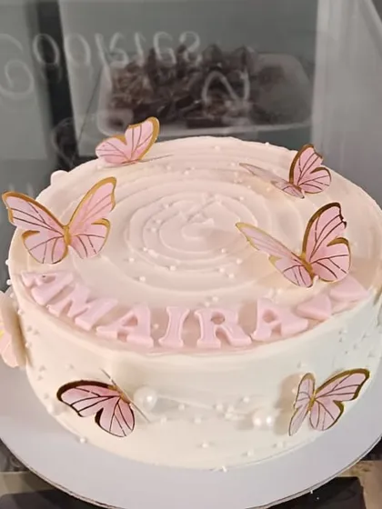 An elegant white cake for Maira, decorated with delicate pink and gold butterflies and pearls.