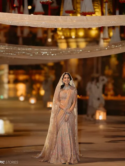 Another angle of Radhika's stunning bridal attire. This shot captures the grandeur of her outfit against the softly lit, ambient background of the celebration.