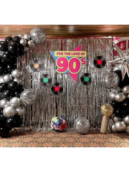 We threw it back with this 'For the love of the 90s' party theme. The decor features a silver fringe backdrop, black and silver balloon columns, disco balls, and vinyl record cutouts to create a fun, retro vibe.