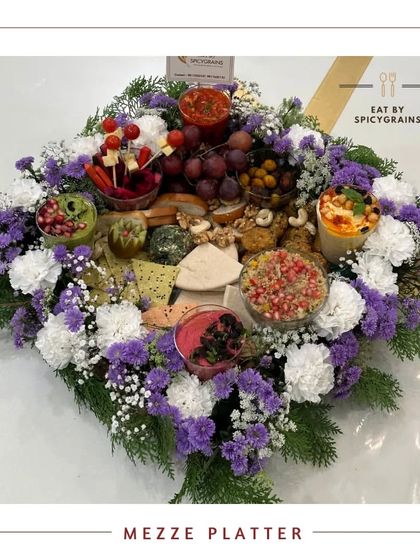 A gorgeous Mezze Platter presented as a floral bouquet. The food is artfully arranged within a bed of fresh flowers, making it an incredibly beautiful and unique centerpiece for a special occasion.