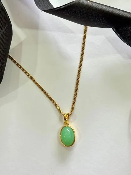 A simple gold chain holds a vibrant green stone, making it a perfect festive pick. This piece adds a touch of color and timeless elegance to any celebration.