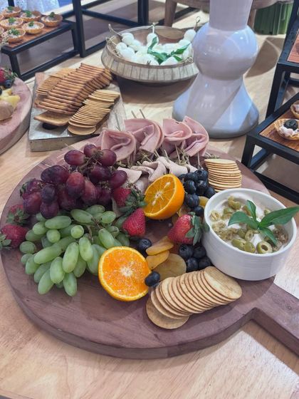 A classic charcuterie board featuring rolled cured meats, a variety of crackers, fresh grapes, berries, and a basil-topped dip. This platter offers a balanced selection of savory and sweet flavors.