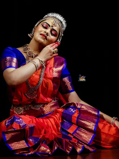 A beautiful seated pose by a classical dancer, with lighting that accentuates the rich colors of her costume and her graceful expression.