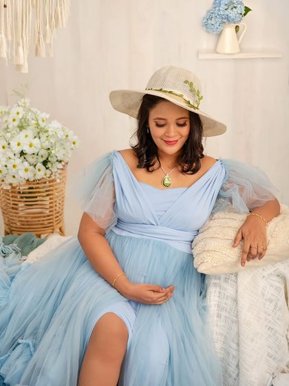 A serene solo portrait. The mother-to-be, wearing a lovely summer hat, relaxes in the cozy, light-filled corner of the blue boho set.