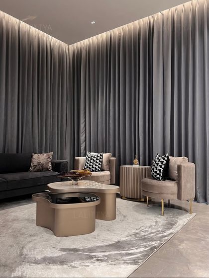A cozy seating nook within the entertainment area, defined by floor-to-ceiling grey curtains. The curved armchairs and abstract-patterned rug create an intimate zone for conversation, away from the main lounge.
