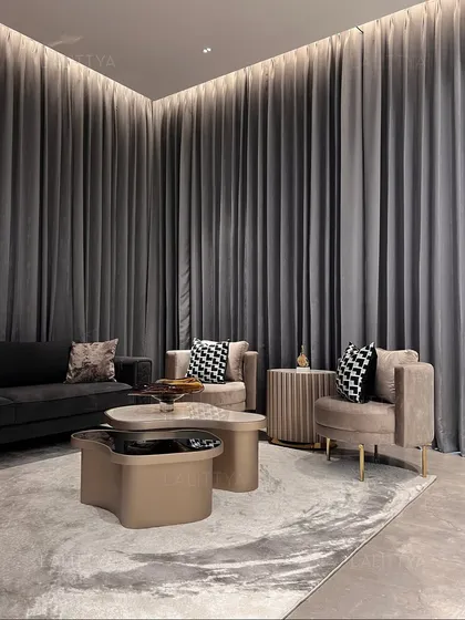 In this entertainment corner, we used dramatic floor-to-ceiling grey curtains to create a cozy, cocoon-like effect. The custom-designed armchairs and uniquely shaped coffee table sit on a textured rug, making it a perfect spot for intimate conversations.