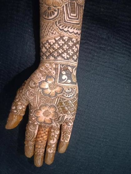 A close-up of a heavy bridal design on the hand, showing a mix of floral and geometric patterns. The fingertips are fully covered, which is traditional for brides.