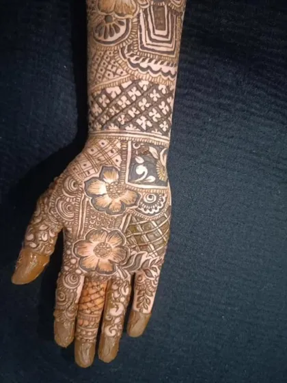 A close-up of a heavy bridal design on the hand, showing a mix of floral and geometric patterns. The fingertips are fully covered, which is traditional for brides.