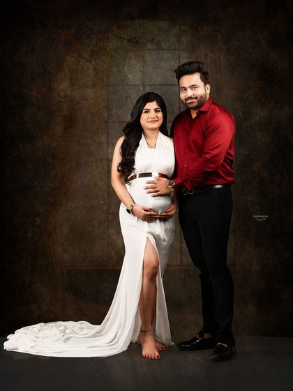 A classic and elegant couple portrait against a dark, textured backdrop. The contrast between her white gown and his red shirt creates a visually appealing and timeless image.