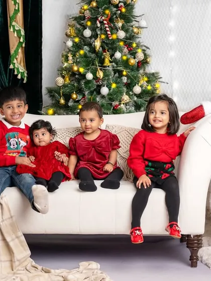 A group of adorable children sitting together on the couch, all dressed in red for their Christmas photoshoot.