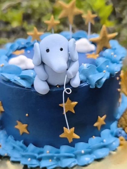 A close-up of the adorable fondant elephant topper, holding a string of stars on this whimsical, galaxy-themed cake.