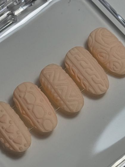 A close-up of the intricate patterns on the sweater nails. Each nail has a different knit design, from classic cables to delicate stitches, all sculpted by hand for a realistic textured effect on these short press-on nails.