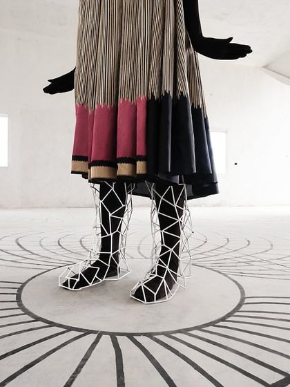 A close-up on custom-designed leg accessories, which encase the model's legs in a geometric web, continuing the campaign's theme of lines and grids.