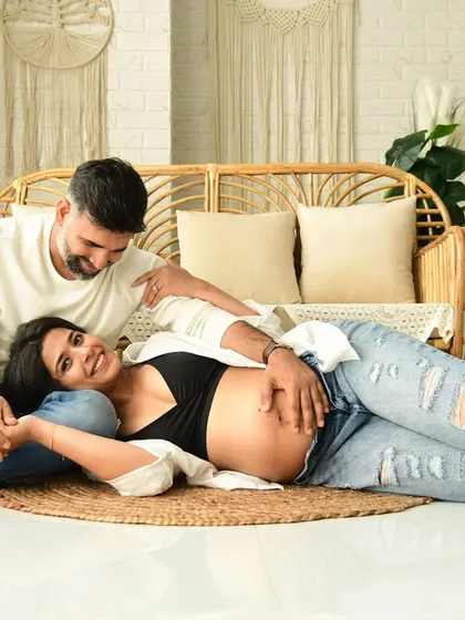 A happy, relaxed portrait of an expecting couple in our boho studio. The natural textures of the rattan furniture and pampas grass complement their casual denim outfits, creating a light and airy feel.