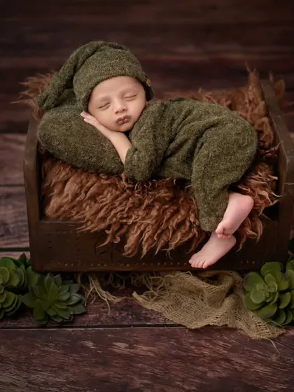 A full view of our little green-clad newborn, sleeping soundly on a rustic wooden bed.