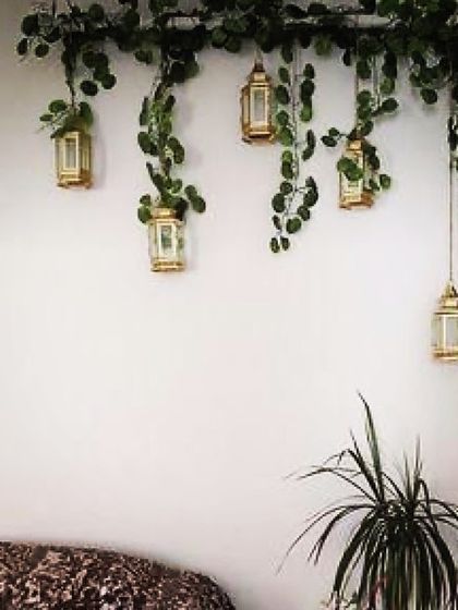A simple yet enchanting wall decor idea. We hung small golden lanterns from a cascade of artificial ivy, creating a whimsical and romantic feature above a seating area that works well both indoors and outdoors.