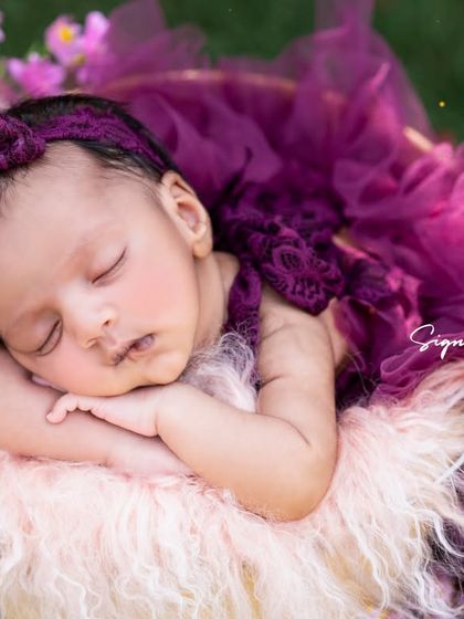A sweet newborn girl napping in a basket, nestled among purple flowers in a beautiful garden setting.