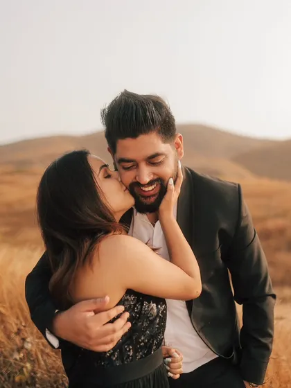 A candid and joyful moment captured in a field of gold. The bride's spontaneous kiss on the cheek shows their playful and affectionate bond.
