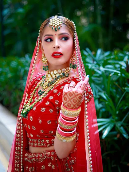 A vibrant outdoor bridal portrait, where the bright red lehenga contrasts beautifully with the green foliage.