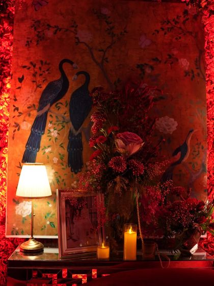 A close-up on a corner of the red lounge, where a beautiful peacock painting is flanked by red floral arrangements and warm candlelight. This detail shot shows how I blend art, light, and florals to create a rich, layered design.